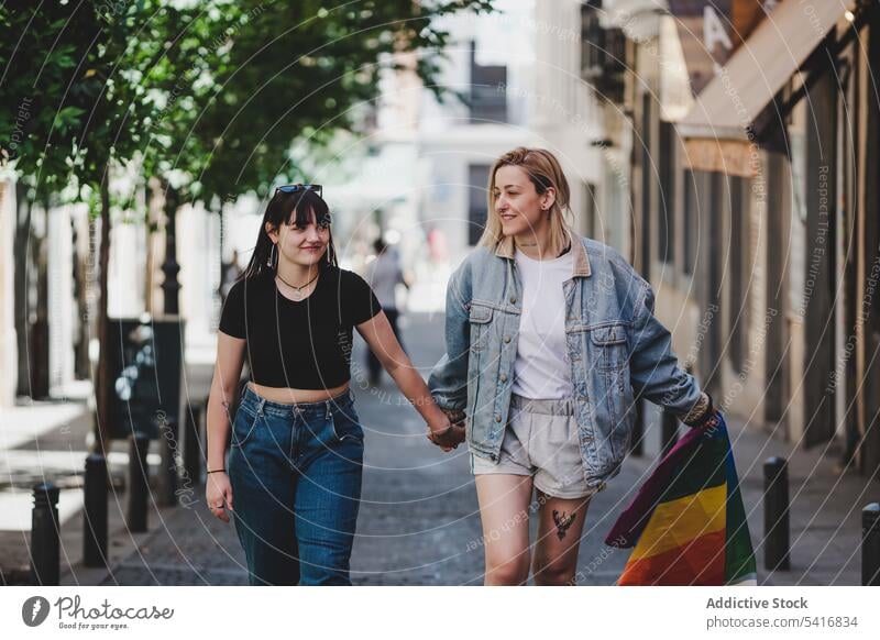 Lesbian couple with LGBT flag walking on street lesbian lgbt happy waving city young together women casual homosexual pride equality alternative relationship