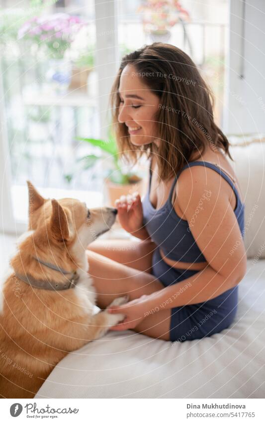 millennial caucasian woman at home with corgi dog. Dog trainer. Funny cozy picture of female with puppy in apartment. Brunette smiling with welsh corgi Pembroke dog sitting on couch.