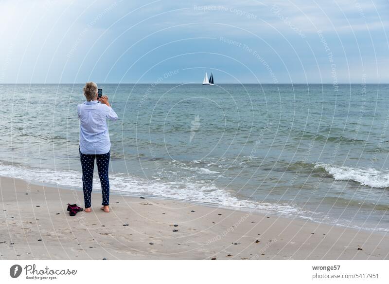 Woman on the beach photographs sailing boats on the Baltic Sea Beach Summer sailboats Taking photos with the phone Take a photo Ocean Sand coast Water Sky