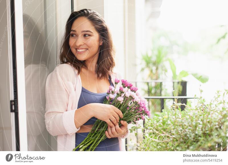 Beautiful woman with flowers bouquet on the balcony. Happy brunette smiling. Plants and flowers gardening hobby. Balcony plant Balcony furnishings Summer