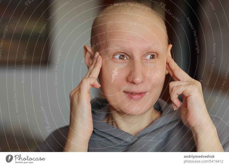Bald woman touching head with fingers, suffering from headache after chemotherapy. Unhappy hairless cancer sick female having migraine at home. Oncology concept. Healthcare,medicine