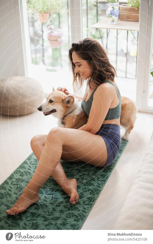 young woman with corgi Pembroke dog doing yoga on green mat at home. Practicing sport, wellness and healthcare. Indoor yoga online class. Mindfullnesss and meditation, active lifestyle.