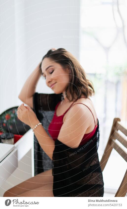 Woman putting on bracelet, getting dressed for party in red and black outfit using fan. Spanish vacation. Passionate sensual romantic female portrait in boudoir room. Summer heatwave.