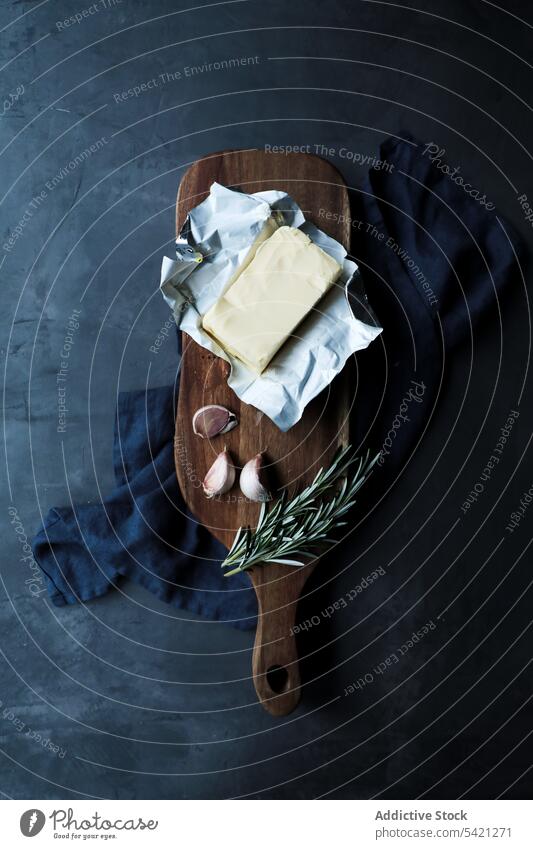 Pack of butter with aromatic seasonings as traditional fresh ingredients for tasty dishes on table rosemary garlic cutting board rustic wooden flavor food dairy