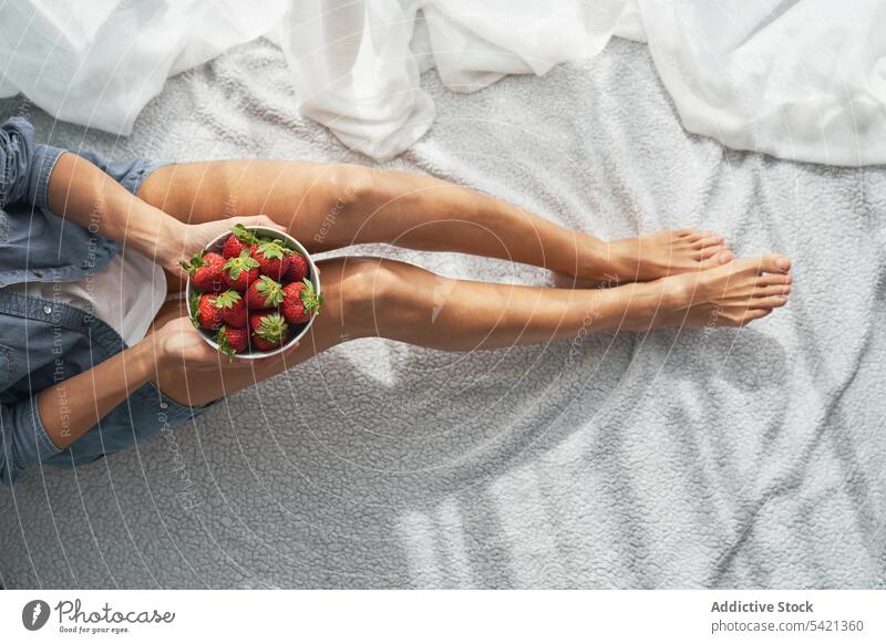 Crop woman with strawberries sitting on bed strawberry bowl home show summer weekend ripe female rest food fruit dessert morning blanket bedroom organic comfort