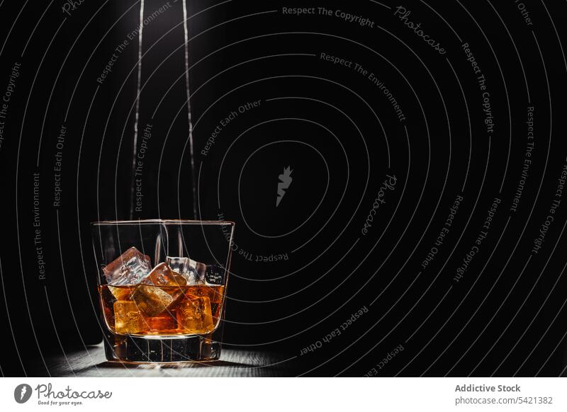 Glass of whiskey with ice cubes in light rays on table in dark room glass scotch bourbon alcohol beverage drink liquid liquor cognac brandy transparent fluid