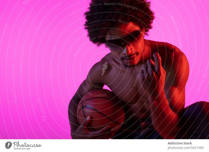Black shirtless man sitting with basketball naked torso muscular sportsman appearance player neon squat male african american black curly hair sunglasses young