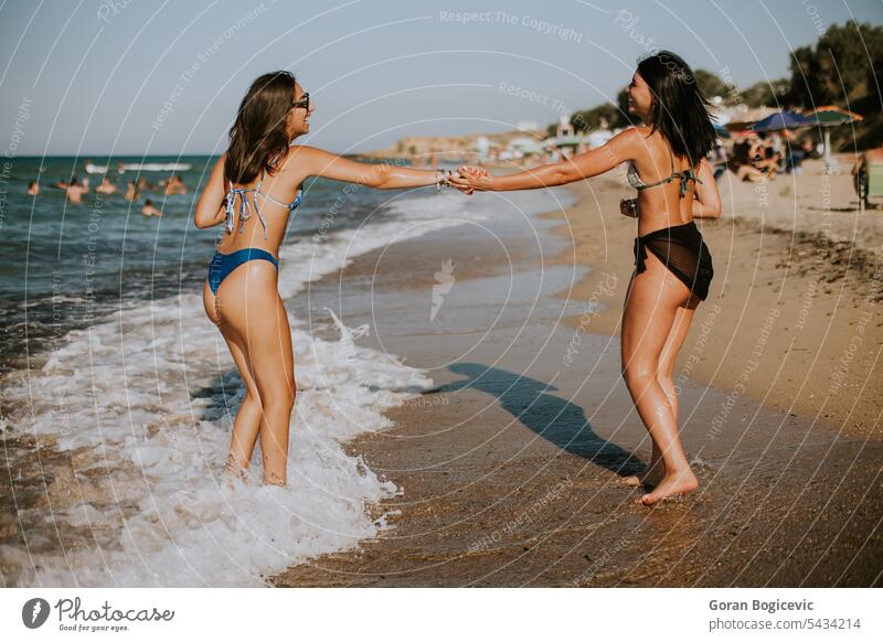 Two pretty young woman having fun on the seaside summer female bikini friends beach vacation swimwear together people happiness sand happy ocean water cheerful