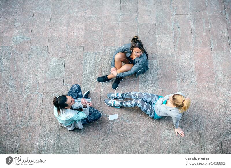 Women friends runners relaxing sitting on the floor after training group women team female resting break talking top view above tired exhausted together