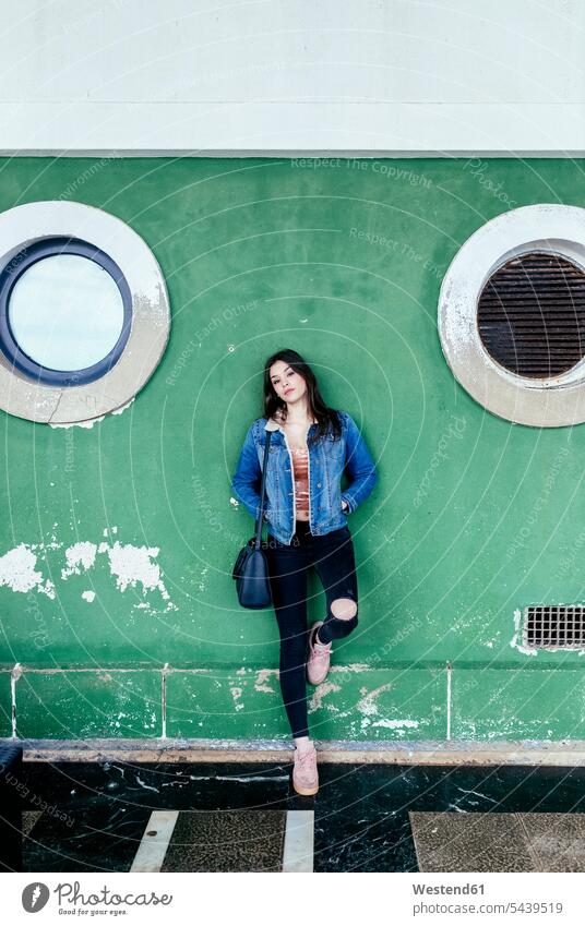 Portrait of a young brunette woman leaning against a green wall standing walls portrait portraits beautiful females women Adults grown-ups grownups adult people