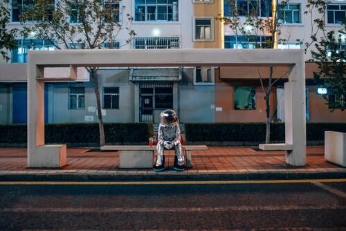 Spaceman sitting on bench at a bus stop at night with soft drink busstops spaceman spacemen by night nite night photography astronaut astronauts