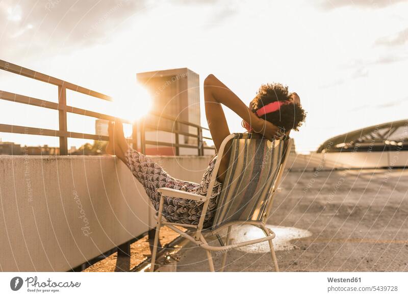 Young woman with headphones sitting on rooftop roof terrace deck Seated hearing relaxed relaxation headset females women music relaxing Adults grown-ups