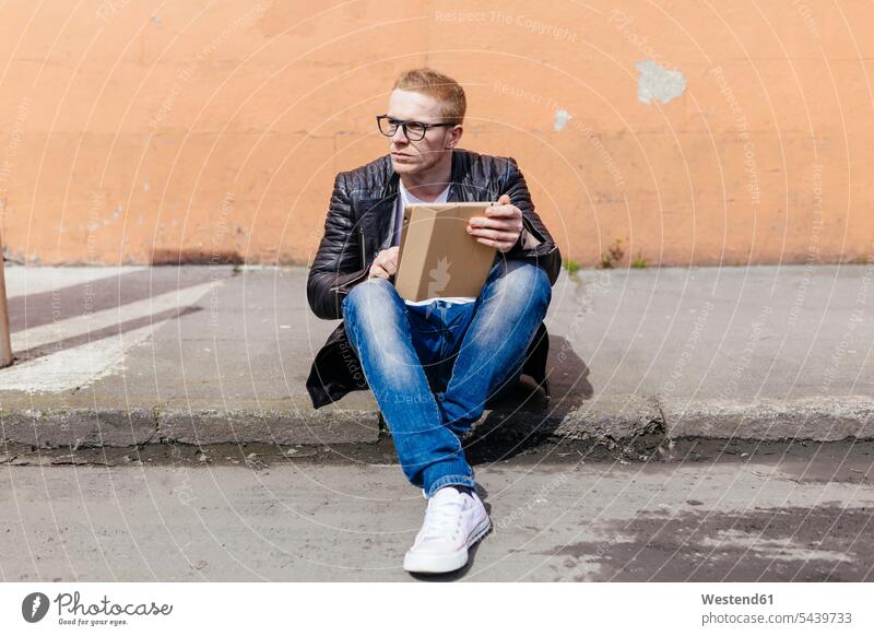 Young man with digital tablet sitting at curb men males Seated digitizer Tablet Computer Tablet PC Tablet Computers iPad Digital Tablet digital tablets Adults