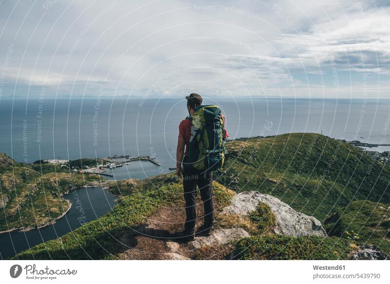 Norway,, Lofoten, Moskenesoy, Backpacker standing on cliff, looking to the Atlantic Ocean Lofoten Islands backpacker Backpackers cliffs ocean oceans Sea water