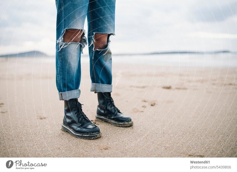 Woman wearing boots and torn jeans on the beach, partial view beaches woman females women tore Denim Jeans standing leg legs human leg human legs Adults