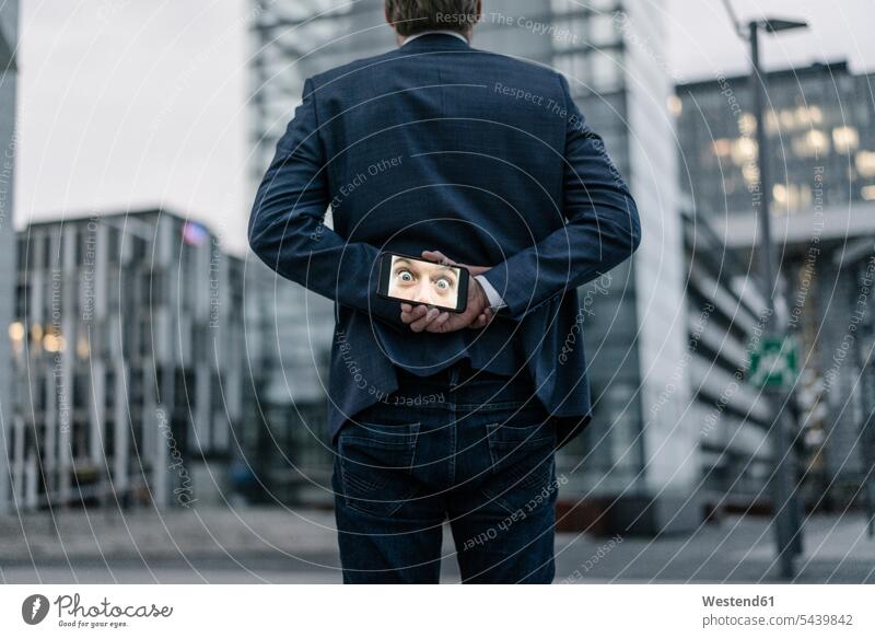 Businessman holding cell phone with image of eyes behind his back photograph photographs photos Business man Businessmen Business men mobile phone mobiles