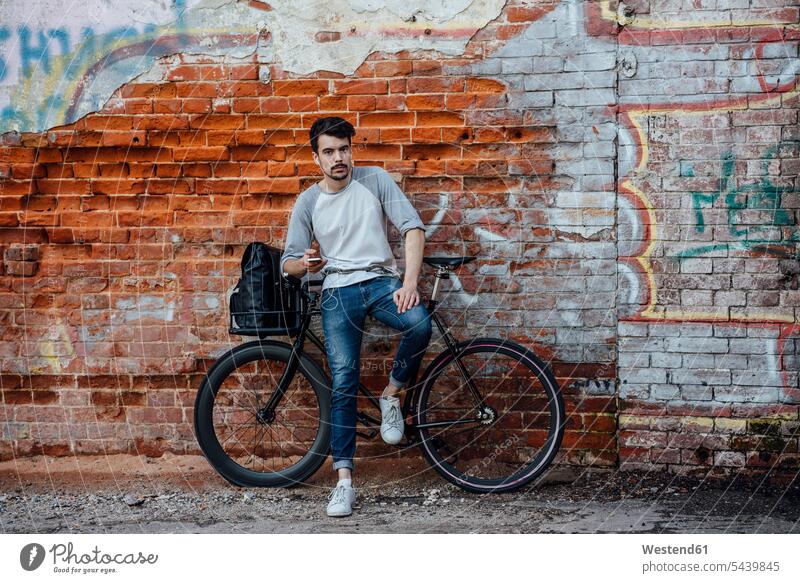 Young man with commuter fixie bike standing at brick wall with cell phone and earphones ear phone ear phones mobile phone mobiles mobile phones Cellphone