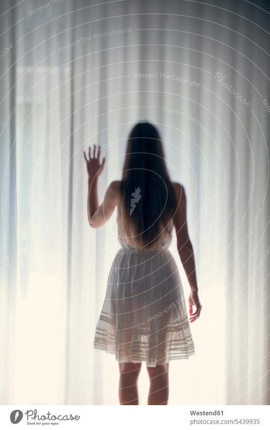 Mystical young woman standing in front of a white curtain, back view young women long-haired long hair longhair long hairs magic supernatural extrasensory