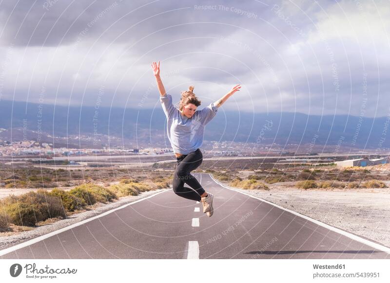Young woman jumping for joy on a road females women streets roads journey travelling Journeys voyage Leaping Adults grown-ups grownups adult people persons