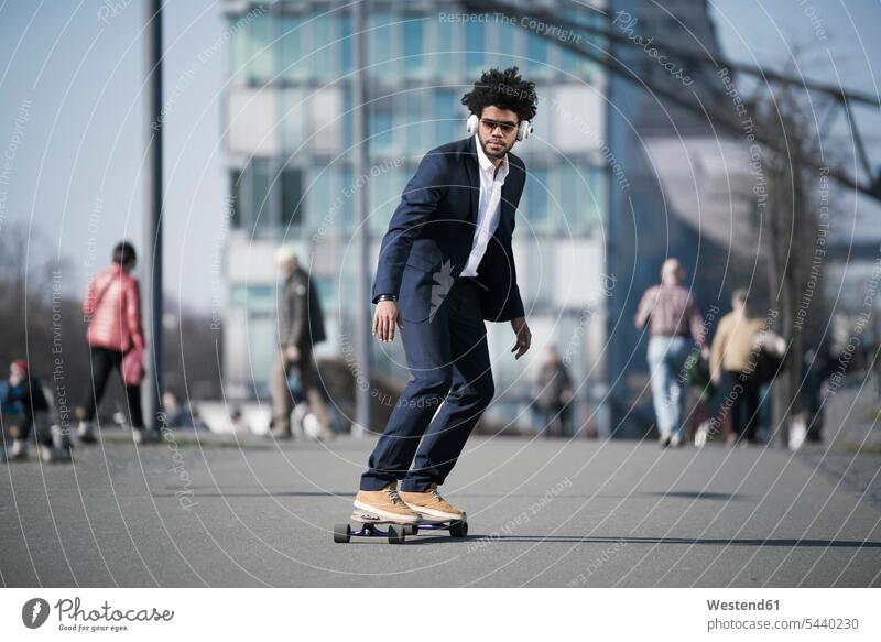 Businessman riding longboard in front of skyscraper men males Business man Businessmen Business men Adults grown-ups grownups adult people persons human being