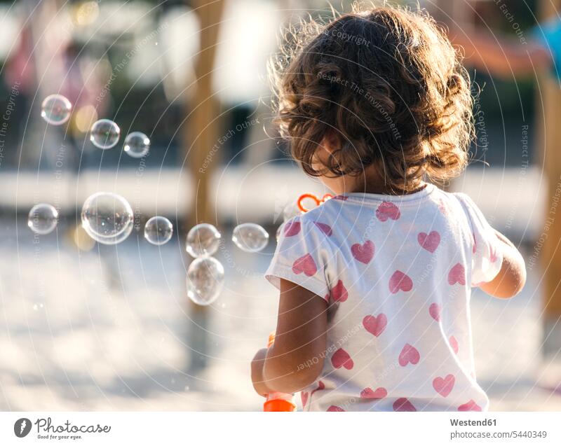 Back view of little girl making soap bubbles at playground - a