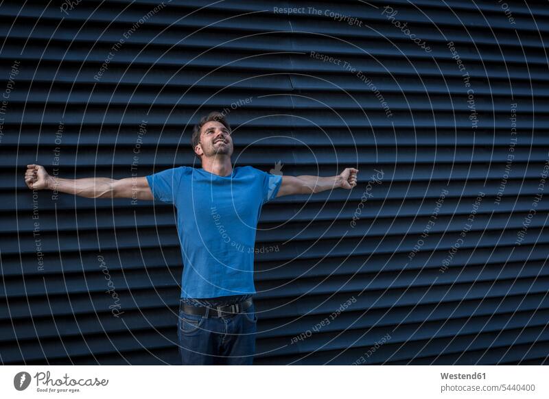Man standing in front of roller shutter, looking up with arms outstretched man men males Anticipation Expectations Anticipating Anticipate hopeful expectation