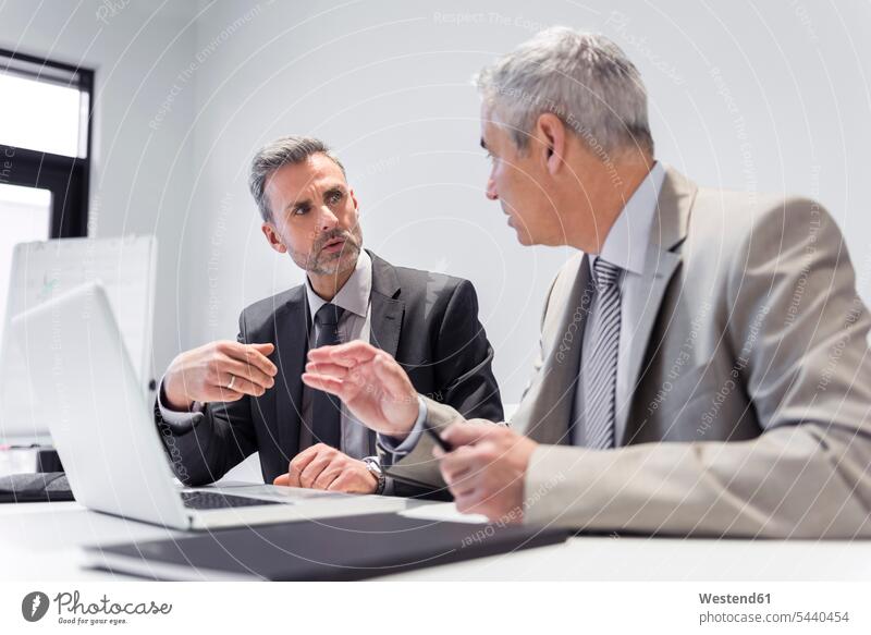 Two businessmen working together in office laptop Laptop Computers laptops notebook At Work sitting Seated offices office room office rooms discussing