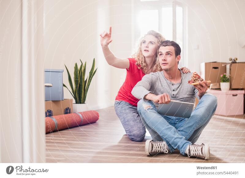 Young couple in new home sitting on floor with tablet twosomes partnership couples flat flats apartment apartments people persons human being humans