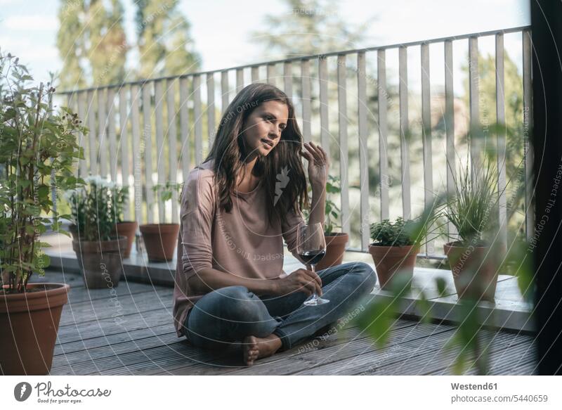 Woman with glass of red wine relaxing on balcony sitting Seated balconies Red Wine Red Wines woman females women relaxed relaxation Alcohol alcoholic beverage