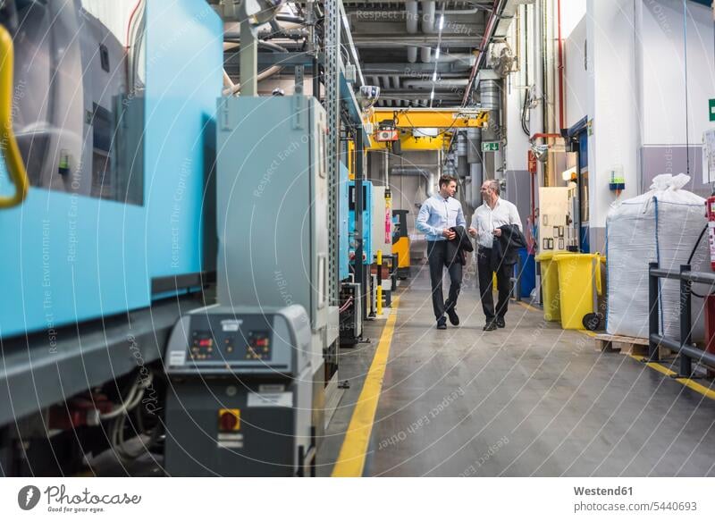 Two men walking and talking in factory shop floor speaking colleagues factories man males Adults grown-ups grownups adult people persons human being humans