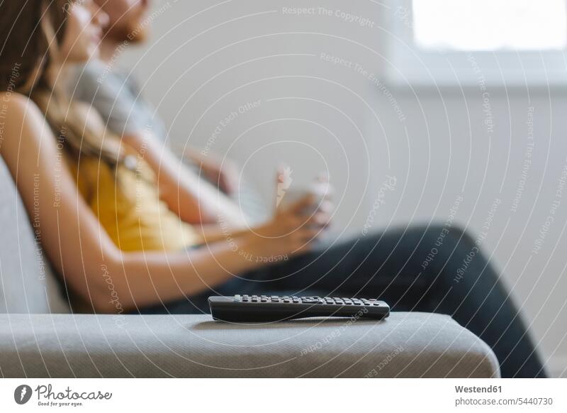 Remote control on backrest with couple drinking coffee and watching TV in the background, close-up Looking At Tv watching television remote control