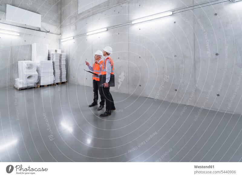 Two colleagues wearing safety vests and hard hats talking in a building working At Work man men males scrutiny scrutinizing Adults grown-ups grownups adult