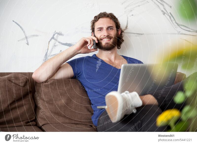 Portrait of young man on the phone sitting on couch in a coffee shop men males portrait portraits call telephoning On The Telephone calling Adults grown-ups