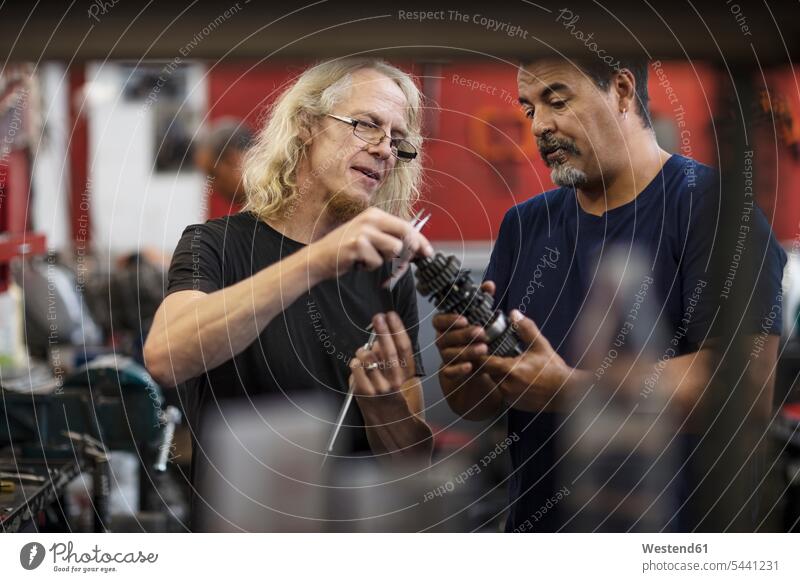 Two mechanics discussing in workshop mechanician repairman mechanicians mechanists repairmen machinists repairing working At Work colleagues industry industrial