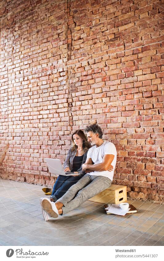 Businessman and woman sitting in a loft, using laptop, founding a start-up company Laptop Computers laptops notebook business people businesspeople startup