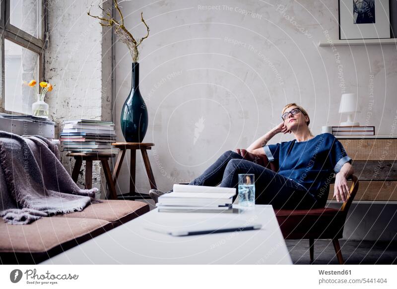 Pensive woman sitting on arm chair in loft looking up lofts freelancer freelancing females women Adults grown-ups grownups adult people persons human being