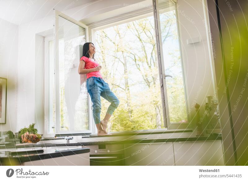 Smiling woman standing in kitchen on windowsill females women Adults grown-ups grownups adult people persons human being humans human beings home at home