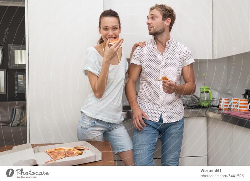 Young couple eating pizza in kitchen Pizza Pizzas domestic kitchen kitchens twosomes partnership couples Food foods food and drink Nutrition Alimentation