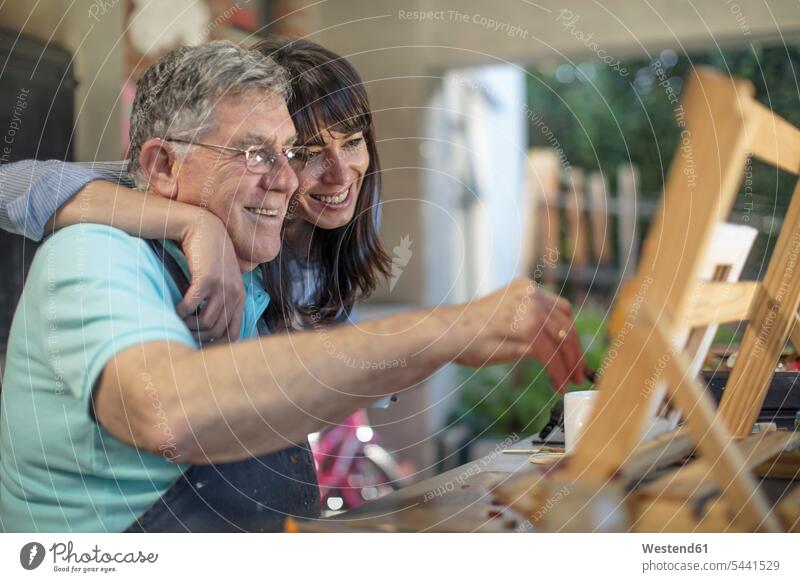 Smiling woman embracing senior man painting senior men elder man elder men senior citizen daughter daughters smiling smile embrace Embracement hug hugging