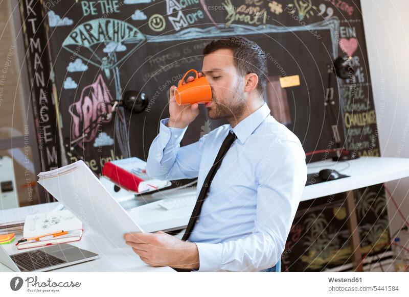Businessman in creative office looking at documents and drinking coffee Coffee Business man Businessmen Business men reading Drink beverages Drinks Beverage
