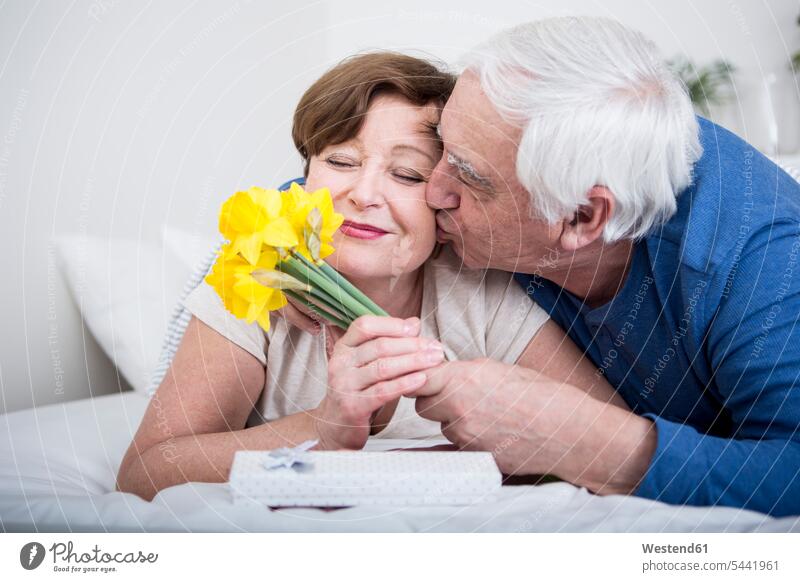 Senior couple lying in bed, man giving bunch of flowers to woman caucasian caucasian ethnicity caucasian appearance european carefree beds relationship