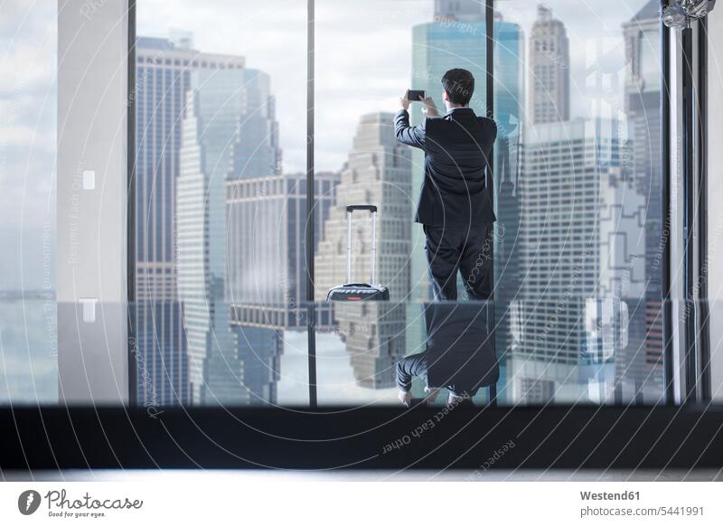 Businessman with rolling suitcase taking photos of city view in office desk desks mobile phone mobiles mobile phones Cellphone cell phone cell phones