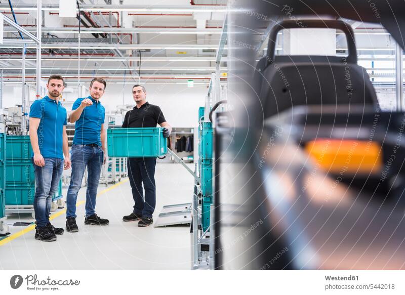 Two men instructing worker with box in industrial hall factory factories man males working At Work colleagues Adults grown-ups grownups adult people persons