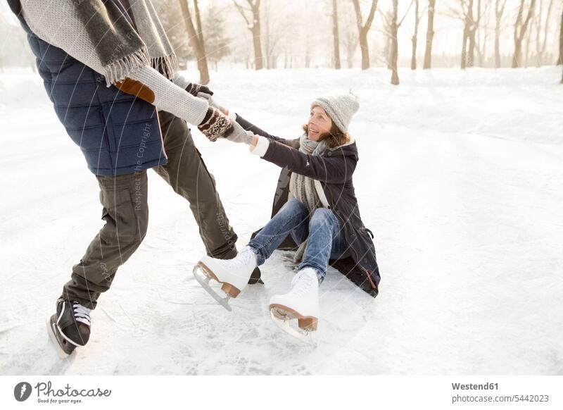 Man helping ice skating woman getting up from frozen lake ice skater skaters ice skaters couple twosomes partnership couples Ice-Skating winter sport