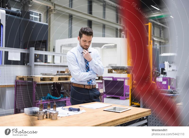 Man at table in factory shop floor thinking factories Businessman Business man Businessmen Business men males business people businesspeople business world