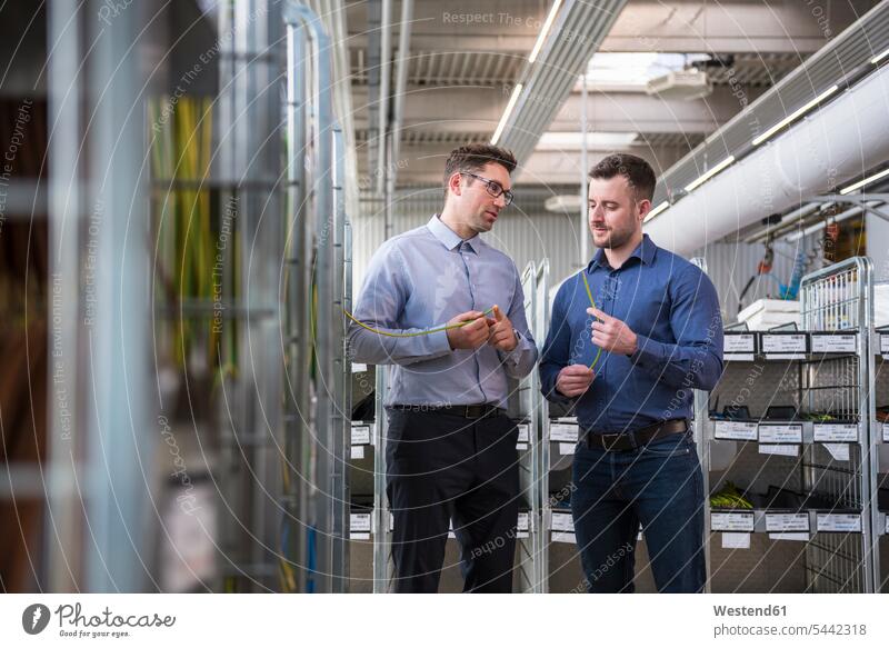 Two men in factory shop floor examining product working At Work man males factories colleagues Adults grown-ups grownups adult people persons human being humans