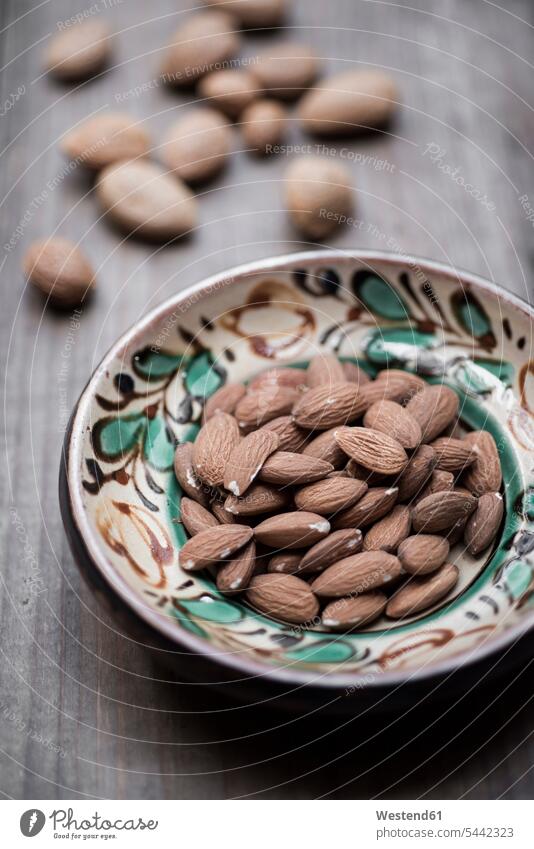 Almonds in hand-painted bowl on wood Nut Nuts close-up close up closeups close ups close-ups large group of objects many objects wooden healthy eating nutrition