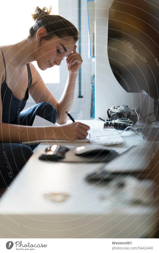 Young woman taking notes at desk female photographer photographs photos writing write females women photographers image images picture pictures Adults grown-ups