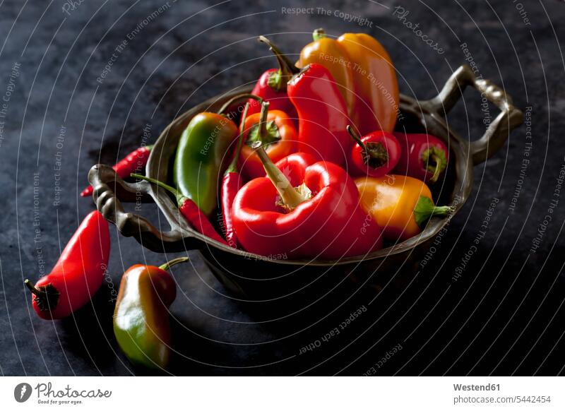 Bowl of various organic bell peppers and chili peppers on dark ground orange hot spicy healthy eating nutrition metal metals yellow diversity abundance