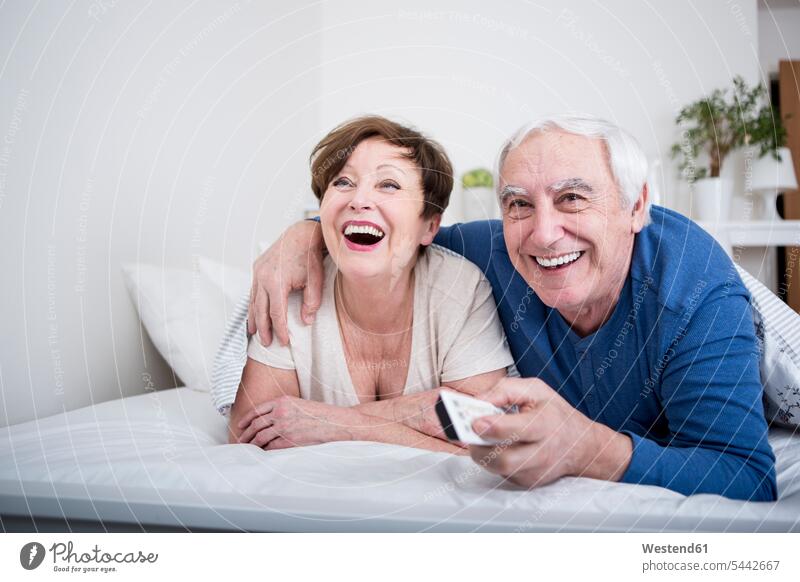 Senior couple lying in bed with remote control caucasian caucasian ethnicity caucasian appearance european carefree beds relationship Human Relationship smiling